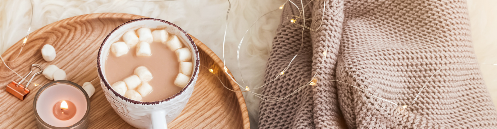 Hot cocoa, a candle, a wood tray, a warm throw blanket in a cozy setting - Celebratopia personalized gifting