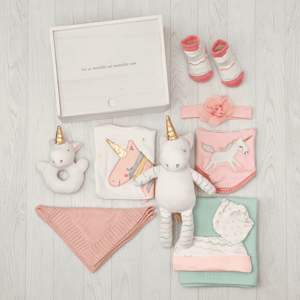 Collection of baby items including a plush unicorn, blanket, and socks on a light wooden surface