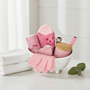 Pink bath accessories including a exfoliating gloves, a lip care kit, a candle and matches, a nail file and pink socks in a mini bathtub shown with a light background
