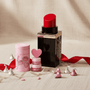 Black lipstick purse with red cap, pink lip care kit cylindrical container, and Hershey's pink and silver chocolate kisses  on a beige surface