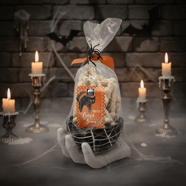 Halloween-themed pretzel bones product packaging held by a hand with candles and cobwebs in the background