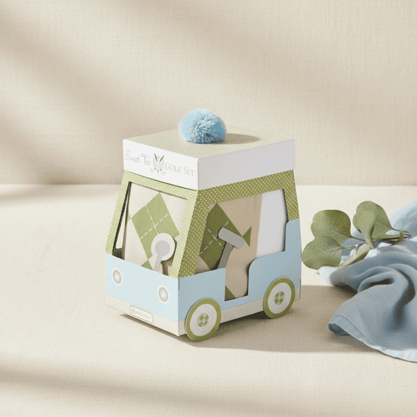 Gift box with a blue pom-pom on top, placed on a beige surface with a light blue napkin.