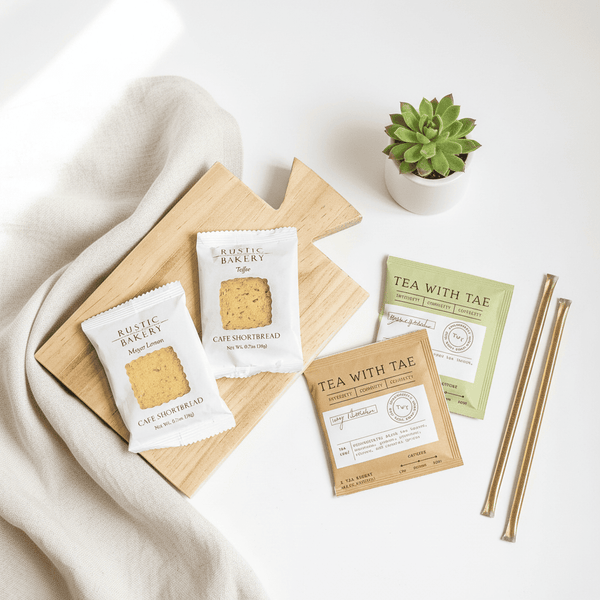 Tea packages, cookies and honey straws on a white surface with a plant in the background