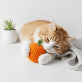Cat playing with a crochet tangerine catnip toy on a white surface