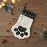 White Christmas stocking with plaid paw design on a wooden surface with festive decorations