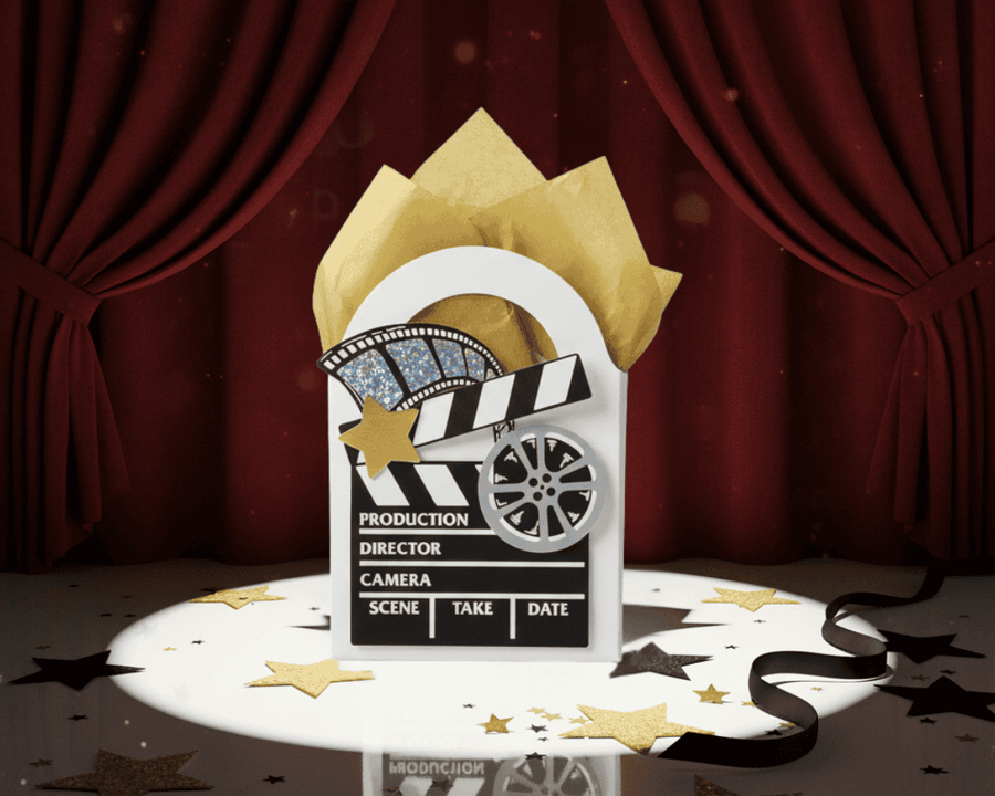 Clapperboard decorated mini gift box with gold tissue paper against a red curtain background