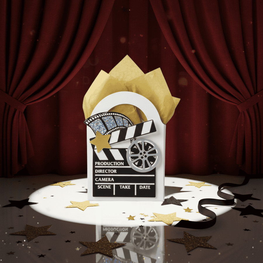 Clapperboard decorated mini gift box with gold tissue paper against a red curtain background