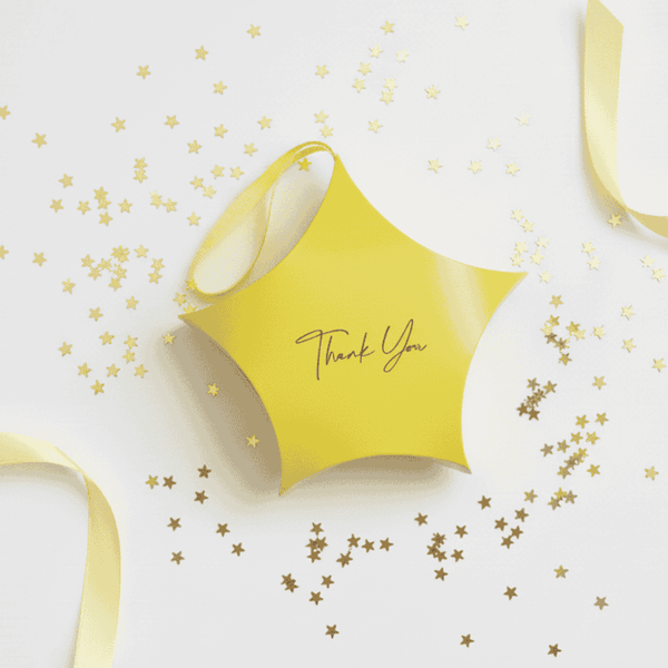 Yellow star shaped gift box with 'Thank You' on the front set on a white background with gold confetti and yellow ribbon