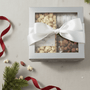 Gift box with a white bow containing snacks on a textured surface with Christmas decorations.